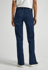 Jeans azul oscuro con corte recto, bolsillos traseros, detalles de diseño mínimos y combinados con zapatillas blancas.