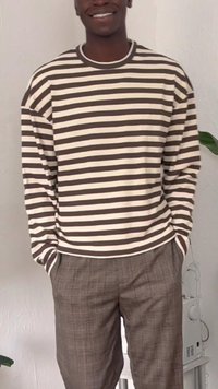 Camisa de manga longa riscada em bege e castanho escuro, combinada com calças xadrez em tons de castanho. Corte casual com bolsos laterais visíveis.