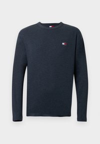 Ilgi piedurkņu tumši zils krekls, kas izgatavots no mīksta auduma ar apaļu apkakli. Uz kreisā krūšu apgabala ir neliela loģotipa birka sarkanā, baltā un zilā krāsā.