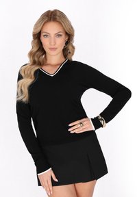Pulover negru cu decolteu în V și mâneci lungi, cu detalii albe la guler și manșete, asortat cu o fustă plisată neagră.