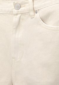 Jean en denim beige avec un design à jambe droite, présentant une fermeture à bouton en métal, des coutures visibles et des poches avant. Détail de texture subtil.