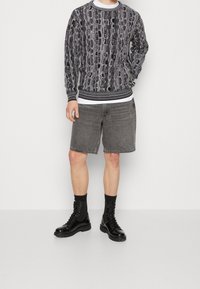 Pullover mit einem schwarzen und weißen, intricaten Muster, runder gerippter Kragen, kombiniert mit grauen Denim-Shorts, schwarzen Schnürstiefeln und Socken.