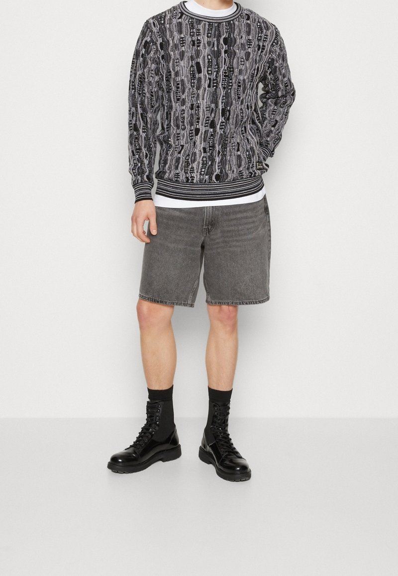 Pullover mit einem schwarzen und weißen, intricaten Muster, runder gerippter Kragen, kombiniert mit grauen Denim-Shorts, schwarzen Schnürstiefeln und Socken.