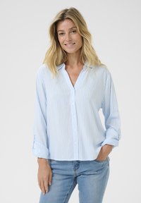 Chemise boutonnée rayée bleu clair et blanche avec un col, des manches longues et une coupe décontractée, associée à un jean bleu.
