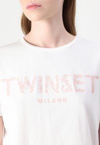 Biela bavlnená tričko s ružovou vyšitou textov "TWINTSET MILANO" s okrúhlym výstrihom a krátkymi rukávmi. Hladká textúra.