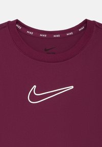 Nike pulkstenis tumši violetā krāsā, ar baltu logotipu priekšējā daļā un ribotu apkakli, kurā iekšpusē atkārtojas "Nike" zīmols.