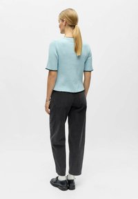 Pull côtelé bleu clair à manches courtes avec bords noirs en forme de vague, associé à un jean ample gris foncé et des chaussures noires.