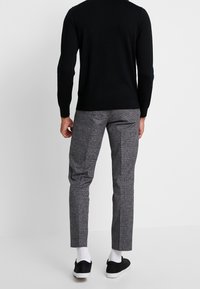 Svart stickad tröja, grå mönstrade byxor, vita strumpor och svarta sneakers. Fokusera på slim fit och strukturerade tyger.