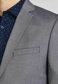 Grå blazer med en glat tekstur, notch lapel og en enkelt brystlomme, parret med en marineblå skjorte med små hvide mønstre.