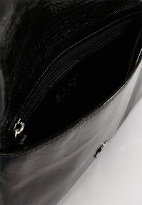 Intérieur d'un sac à main en cuir noir avec une texture lisse, comportant une poche zippée et une petite étiquette de logo visible à l'intérieur.