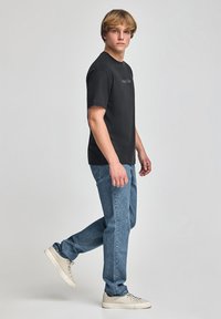 Svart bomullströja med rund hals och korta ärmar, med diskret text "Polo Club", ihop med ljusblå jeans och neutrala sneakers.