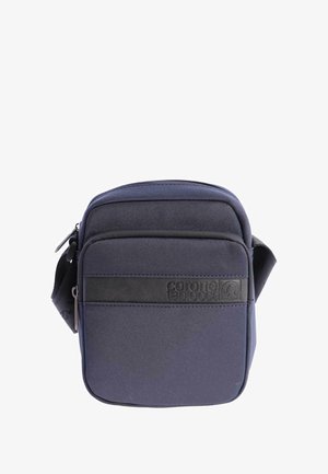 Bolso cruzado compacto de color azul oscuro con bolsillo frontal con cremallera y correa ajustable negra, que presenta un logo en relieve de "coronel tapiocca".