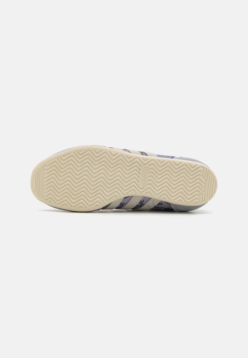 Sneaker viola e grigia con una tomaia testurizzata, caratterizzata da tre strisce bianche e una suola in gomma decorata con battistrada a spina di pesce.