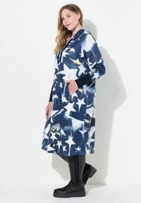 Huvtröja i marinblå fleece med stjärnmönster. Har framfickor och kontrasterande svarta muddar. Kombineras med knähöga svarta stövlar.