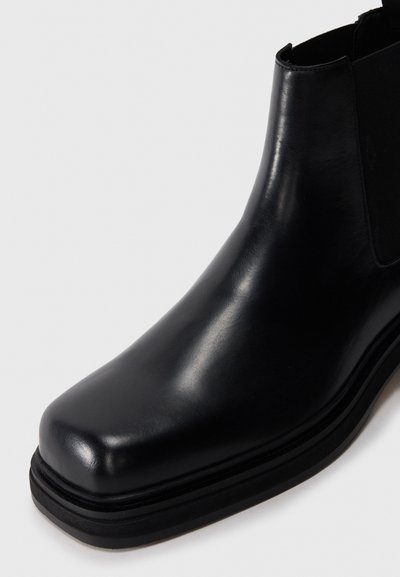 Black leather ankle boot with square toe, elastic side panel, and layered sole on a white background.