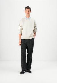Pullover de lã bege claro com um decote redondo e uma camisa de colarinho azul por baixo, combinado com calças escuras e ajustadas e ténis pretos.
