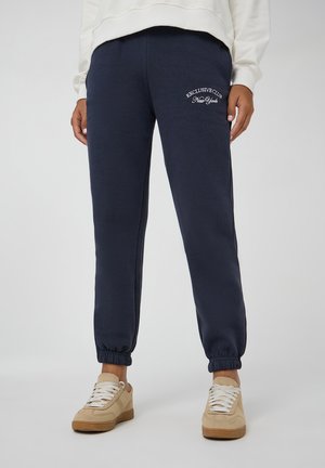 Pantaloni jogger blu navy realizzati in tessuto morbido, con vita elastica, regolati alla caviglia, caratterizzati da testo ricamato bianco sulla coscia.