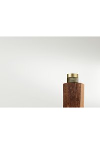 Groene crèmela met gouden deksel tentoon gesteld op een gestructureerde houten verhoging. Gladde oppervlakken contrasteren met de ruwe houtnerf.