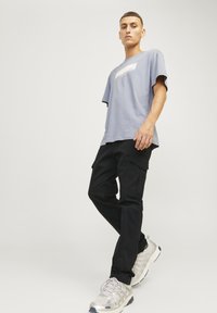 Camiseta gris claro con un logo blanco, combinada con pantalones cargo negros con bolsillos y un corte recto, complementados con zapatillas grises.