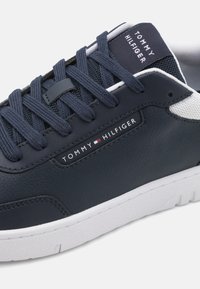 Marinblå sneakers i syntetiskt läder med strukturerad yta, vita detaljer och platta snören. Har en logotag på sidan och vadderad krage.