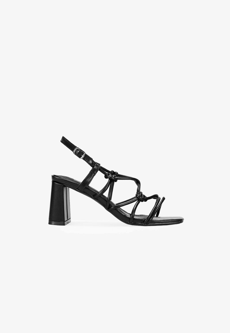 Sandale à talons noirs avec un design à lanières, des détails noués, une bride de cheville ajustable et un talon carré pour plus de stabilité.