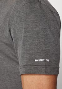 Camiseta gris de manga corta con una textura suave. Presenta un logo blanco "DRYFLIGHT" en el hombro izquierdo. Diseño simple y ajustado.