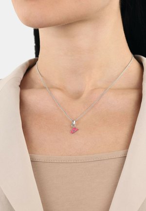 Silberne Kettenhalskette mit einem rosa Charme, der einem Hut ähnelt, mit kunstvollen Details. Getragen zu einem Oberteil in neutralen Farbtönen.