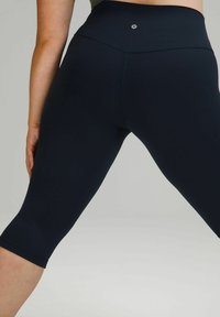 Leggings cropped taille haute, bleu marine, en tissu extensible avec une texture lisse et un matériel minimal, avec un petit logo sur la ceinture.