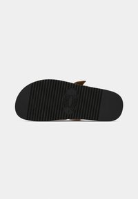 Brun sandal med en sort gummisål, der har vandrette riller for bedre greb. Designet inkluderer en strop til lukning på toppen.