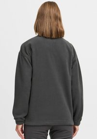 Grå fleecetrøje med afslappet pasform, rund halsudskæring og lange ærmer. Har ribkanter ved ærmegab og kant. Blød, tekstureret overflade.