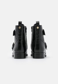 Botas negras de piel hasta el tobillo con textura de cocodrilo, acentos en hardware dorado y doble cremallera lateral. Tacones ligeramente elevados.