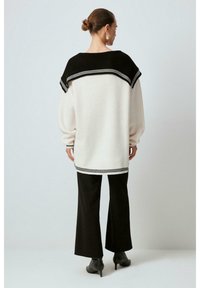 Maglione crema con dettagli neri, scollatura ampia, spalle scese e bordi a coste; abbinato a pantaloni neri a zampa d'elefante e stivali con tacco.