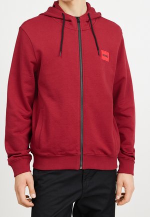 Rode zip-up hoodie gemaakt van soepel materiaal met een voorzak, zwarte trekkoorden, ribbels aan de mouwen en een merklabel op de borst.
