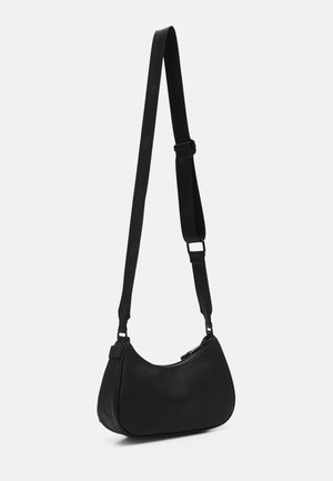 Czarna torebka na ramię w kształcie półksiężyca z regulowanym szerokim paskiem i górnym zamkiem błyskawicznym, wisząca na białym tle.