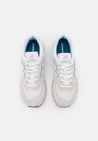 Zapatillas New Balance blancas con materiales de malla y ante, que presentan una puntera redonda, sistema de cordones en la parte delantera y un forro interior azul. Estilo 574.