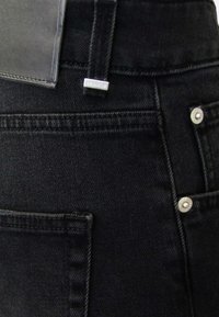 Jeans in denim nero con vita alta, cuciture visibili, due tasche posteriori e accenti in metallo. Etichetta piatta in pelle attaccata.