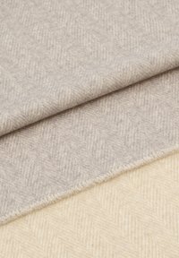 Tissu à motif chevron gris clair et crème, tissé avec une texture douce, bords effilochés, présentant deux couches superposées.