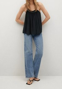 Schwarzes ärmelloses Top mit gerafftem Stoff und Perlenakzenten am Ausschnitt, kombiniert mit hellblauenweiten Jeans und schwarzen Flip-Flops.