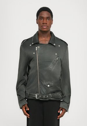 Schwarze Motorradjacke aus Stoff mit diagonalem Reißverschluss, großen Reverskragen und mehreren mit Reißverschluss versehenen Taschen. Verfügt über metallene Druckknöpfe und einen taillierten Bund.