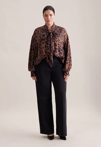 Leopardenmuster-Bluse mit Schleife am Kragen, kombiniert mit schwarzen, weit geschnittenen Hosen. Glatter Stoff mit langen Ärmeln.