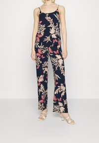 Ensemble floral à deux pièces avec un fond bleu marine, présentant des motifs botaniques roses et blancs sur un top sans manches et un pantalon large.