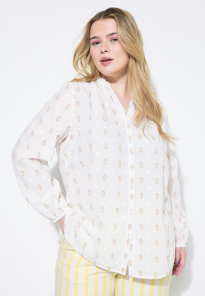 Blusa bianca con un delicato motivo floreale in arancione e oro. Presenta una chiusura a bottoni e una vestibilità comoda, con maniche lunghe leggermente a sbuffo.