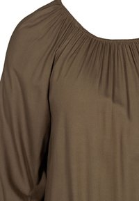 Blouse marron avec encolure froncée et tissu texturé, avec une coupe ample et des manches fluides. Détail mettant en valeur la structure drapée.