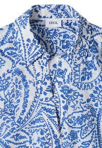Chemise blanche avec motifs floraux et cachemire bleus complexes, dotée d'un col et d'une étiquette de marque "CECIL" à l'intérieur.