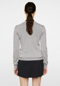 Harmaa neulepusero pitkillä hihoilla, resorireunoilla ja helmalla. Yhdistetty mustan hameen kanssa, kuvattu takaa. Sujuva rakenne, minimalistinen muotoilu.