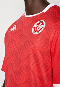 Punane jalgpallijersey, millel on tekstureeritud muster, valge kaeluse ja varrukate aktsendid ning jalgpalliföderatsiooni logo vasakul rinnal.