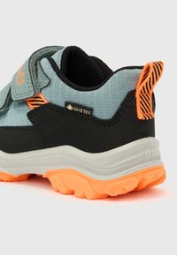 Παιδικό παπούτσι Gore-Tex σε γκρι και μαύρο χρώμα με έντονη πορτοκαλί σόλα και θηλιά για να το τραβάει κανείς, με λουράκι βέλκρο και επένδυση υποστήριξης στον αστράγαλο.