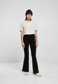 Camiseta cortada de color beige claro con mangas cortas, combinada con pantalones de campana negros. La modelo lleva un gorro negro y zapatillas blancas.