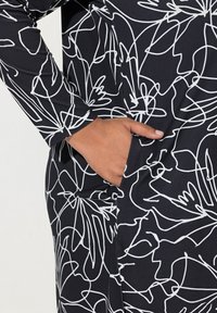 Vêtement noir à manches longues avec des motifs floraux abstraits en ligne blanche. Comprend une poche latérale et une texture de tissu lisse et extensible.