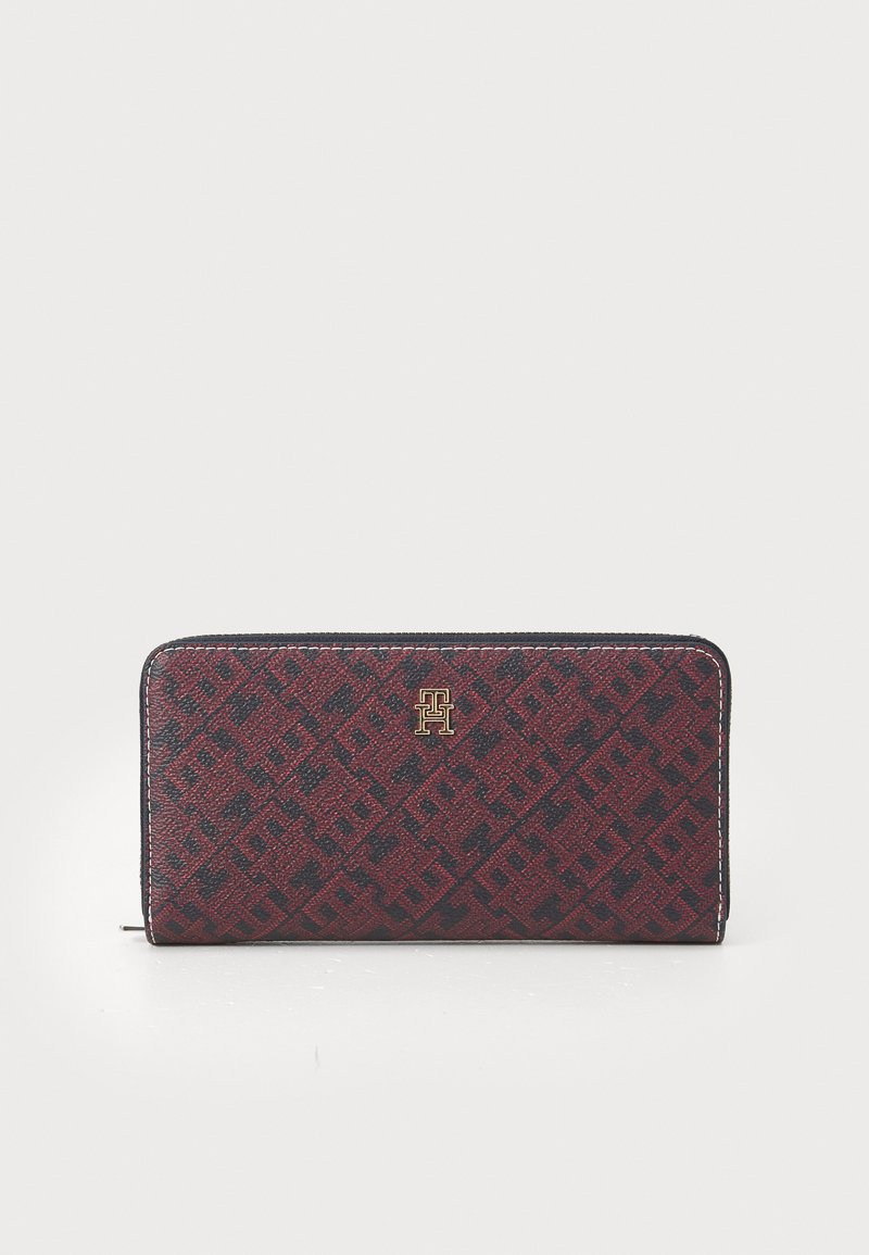 Red and navy patterned wallet with a textured exterior, featuring a gold logo accent. Secured by a zip closure along the sides.